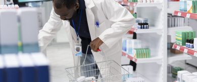 African American pharmacist organizing pharmacy shelves with medication, checking packaging and controlling stock levels to ensure order, cleanliness and efficiency in the pharmacy interior.