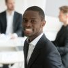 Smiling attractive young african american businessman in suit looking at camera, headshot vertical portrait of black professional executive manager posing with business partners team at background